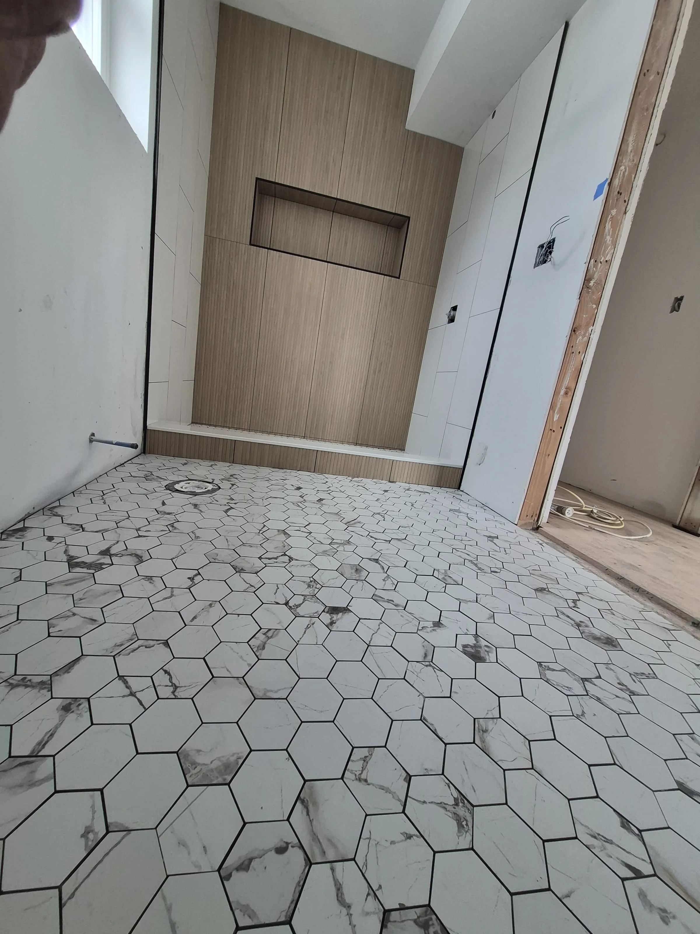 Wood-paneled walk-in wet room — wood-grain porcelain accent wall, built-in bench, recessed niche, hex marble floor
